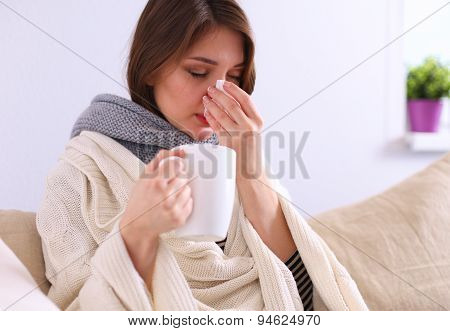 Portrait of a sick woman blowing her nose while sitting on the sofa