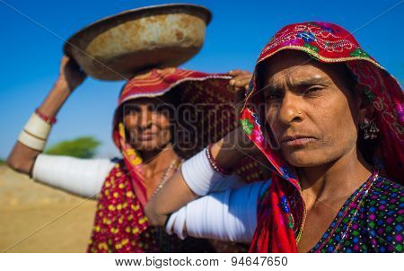 GODWAR REGION, INDIA - 14 FEBRUARY 2015: Rabari tribeswomen stand in field wearing sarees and upper-arm bracelets. One balances bucket on head. Rabari are an Indian community in the state of Gujarat.