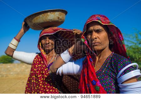 GODWAR REGION, INDIA - 14 FEBRUARY 2015: Rabari tribeswomen stand in field wearing sarees and upper-arm bracelets. One balances bucket on head. Rabari are an Indian community in the state of Gujarat.