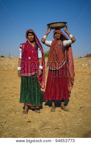 GODWAR REGION, INDIA - 14 FEBRUARY 2015: Rabari tribeswomen stand in field wearing sarees and upper-arm bracelets. One balances bucket on head. Rabari are an Indian community in the state of Gujarat.