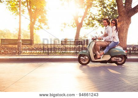 Cheerful young couple riding a scooter and having fun. Sun is shining in the morning