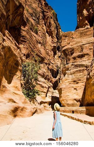 Photo of the Stylish female tourist in trendy hat and sky-blue dress explore canyon Siq leading to The Treasury, Al Khazneh. Travel and adventure concept.