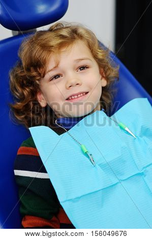 baby boy with curly red hair in blue dental chair. Children's dentist