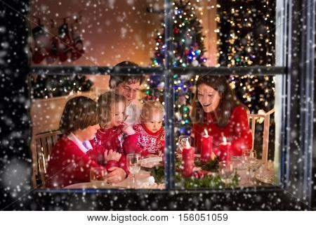Big family with three children celebrating Christmas at home. Festive dinner at fireplace and Xmas tree. Parent and kids eating at fire place in decorated room. Child lighting advent wreath candle.