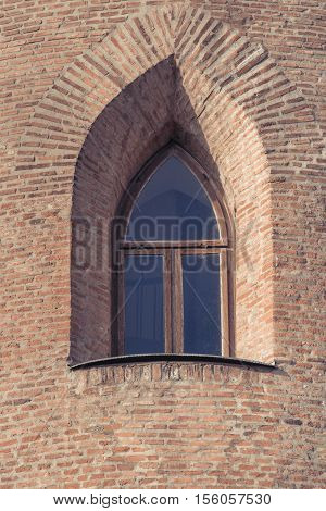 Window in old citadel. Old window in the wall of a medieval building in Europe. Window in old brick wall ruins of a medieval fortress. Old arched without glass window in a brick wall.