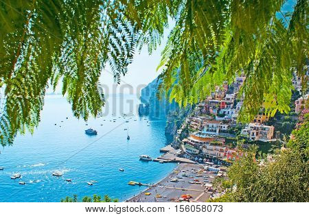 The villas and cottages of old Positano its rocky coast with medieval towers beach Marina Grande harbor through the shady green branches of acacia Italy.