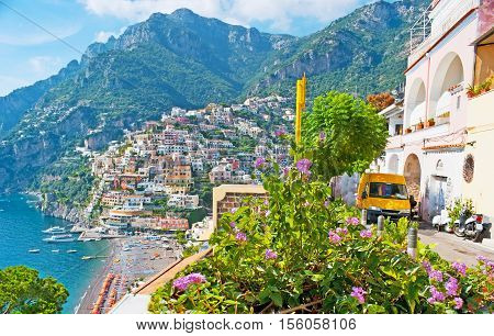 The with old colorful villas of Positano and the comfortable sand beach are seen behind the bright flower shrub Positano Italy.