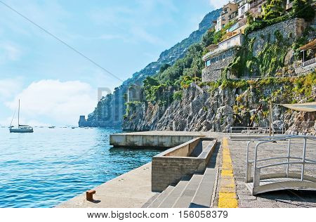 The sea promenade of Positano is the best place to discover the indented coast huge rocks old villas on the slopes ruins of the medieval watch towers yachts and fishing boats in harbor Italy.