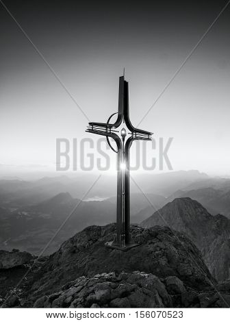 Steel Crucifix At Mountain Peak In Alps. Sharp Rocky Summit, Daybreak Sun In Sky.