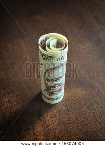 Rolled One thousand rupee note placed on wooden background.