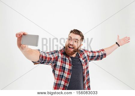 Portrait of a cheerful happy man taking selfie with raised hand over white background