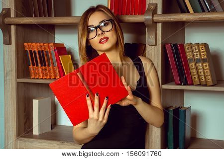 cute librarian reads a book with glasses in the library next to the bookshelf