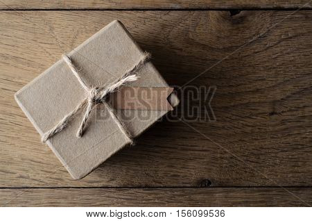 Overhead shot of a simple rustic plain brown gift box tied with string and a blank tag for copy space Set on old Oak wood planking.