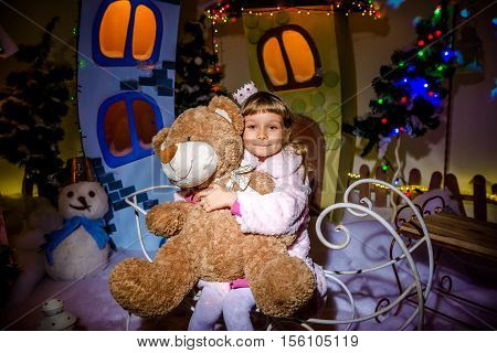 Very nice beautiful long-haired well-dressed attractive little girl with a big bear brown sledging cool photo-studio with great amount of winter new-year's decoration Christmas night