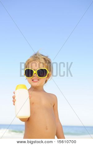 bambino con occhiali da sole mostrando sunblock in spiaggia