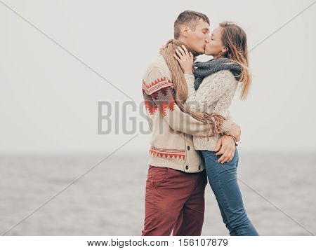 Young attractive couple in knitted sweaters on a cliff on sea shore kissing creative toning