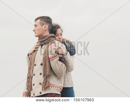 Young attractive couple in knitted sweaters on a cliff on sea shore hugging and holding hands creative toning