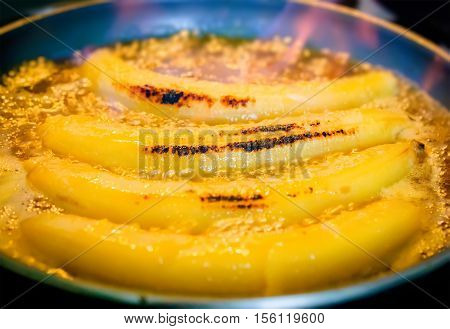 Bananas flambe with orange flame of burning rum cooking process. Selective focus on the central banana.