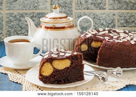 Baking in multicooker. Delicious homemade chocolate cake with curd-coconut balls on a blue wooden table. Decorated with coconut crunch. Served with tea. Selective focus