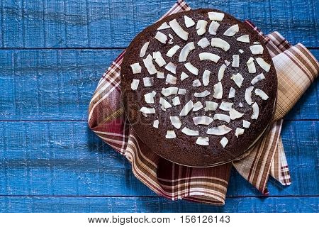 Baking in multicooker. Delicious homemade chocolate cake with curd-coconut balls on a blue wooden table. Decorated with coconut crunch. Top view