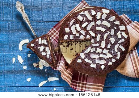 Baking in multicooker. Delicious homemade chocolate cake with curd-coconut balls on a blue wooden table. Decorated with coconut crunch. Top view