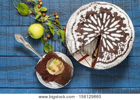 Baking in multicooker. Delicious homemade chocolate cake with whole apples curd and candied fruit on a blue wooden table. Top view