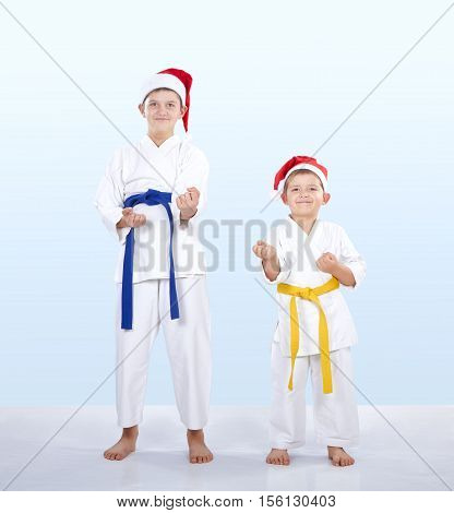 Younger and older brother in caps of Santa Claus standing in the rack of karate