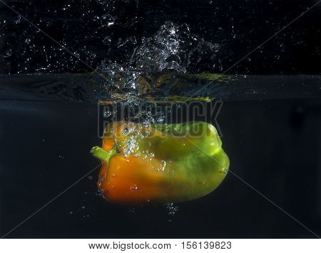 An orange and green pepper splashing in the water