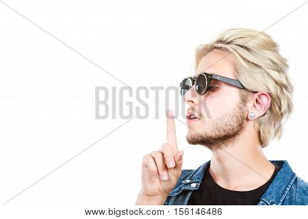 Men fashion accessories hairstyle modeling concept. Artistic hipster blonde man wearing sunglasses showing silence gesture finger on lips profile portrait studio shot isolated