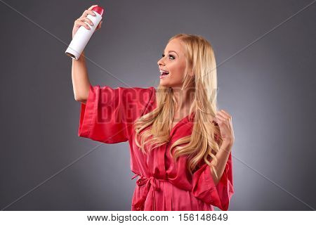 A beautiful young woman wearing a pink robe and smiling while using a hairspray