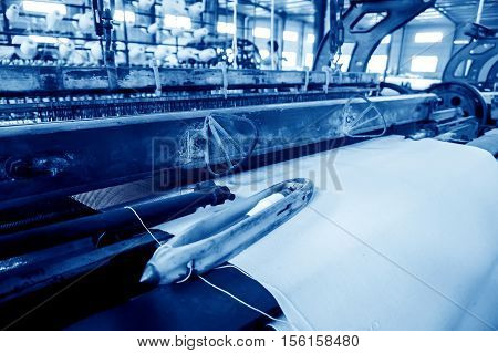 A row of textile looms weaving cotton yarn in a textile mill.