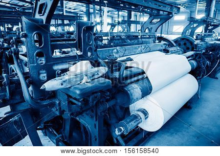 A row of textile looms weaving cotton yarn in a textile mill.