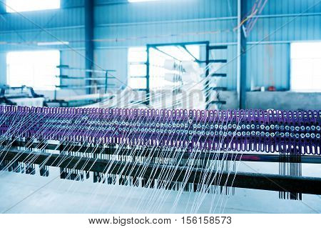 A row of textile looms weaving cotton yarn in a textile mill.