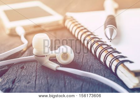 White Headphones, Smartphone With Notebook On Wood Table Background Vintage Color.