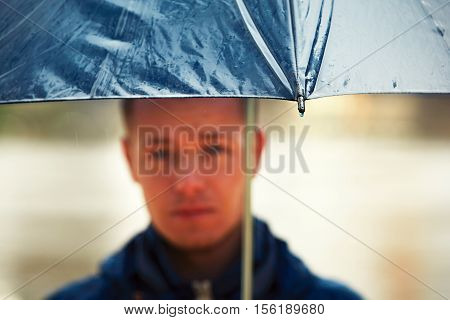 Rainy day. Young man is holding blue umbrella and walking in rain. - selective focus on the drop