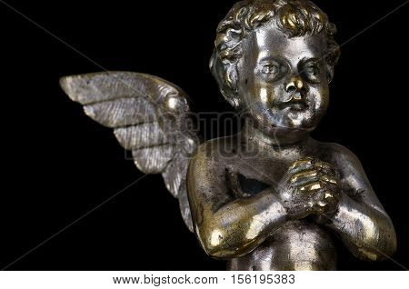 Praying winged putto side view on black background. Angel made of brass, covered with silver, part of a candelabra from nineteenth century. Symbol for religious passion. Macro object photo front view.