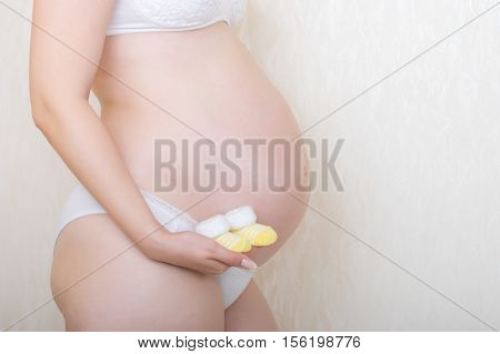 Indoor shpt of pregnant woman holding booties on belly background
