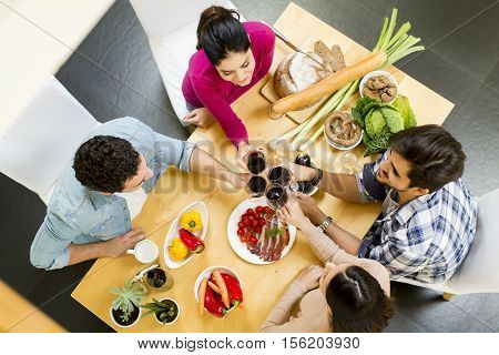 Group of happ young people sitting by the table eating and drinking red wine