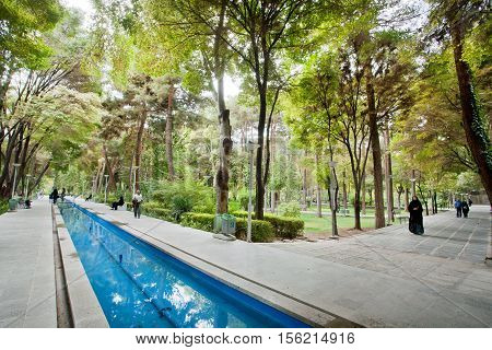 ISFAHAN, IRAN - OCT 16, 2014: Women and men walking near the water ditch in a city park with green trees on October 16, 2014. Third largest city in Iran Isfahan is outstanding example of Islamic culture