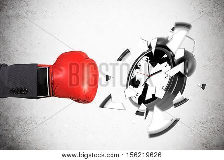 Businessman's hand in red boxing glove is smashing giant alarm clock against concrete wall. Concept of deadline.