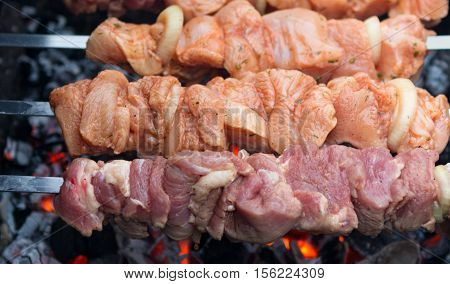 grilled meat over the coals on a barbecue. Raw skewered marinated chicken and pork. Uncooked marinated shish kebabs for grilling in BBQ
