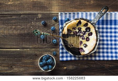 Fresh homemade Dutch Baby pancake with blueberries in iron skillet sprinkled with powdered sugar on rustic wooden background. Top view.