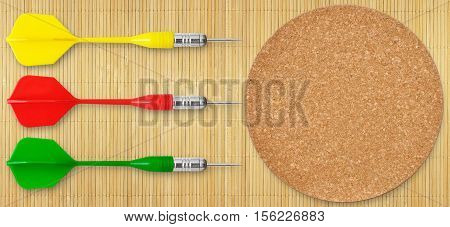 Three colored darts and a cork circle on the background of mat of bamboo