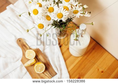 Simply stylish wooden kitchen with bottle of milk and glass on table, summer flowers camomile, healthy foog moring concept noone