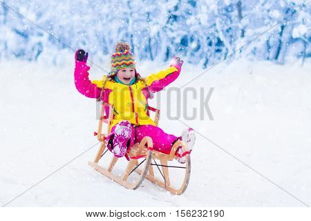 Little girl enjoying a sleigh ride. Child sledding. Toddler kid riding a sledge. Children play outdoors in snow. Kids sled in the Alps mountains in winter. Outdoor fun for family Christmas vacation.