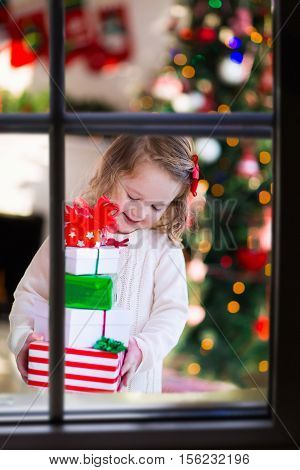 Family on Christmas morning at fireplace. Kids opening Xmas presents. Children under Christmas tree with gift boxes. Decorated living room with traditional fire place. Cozy warm winter day at home.