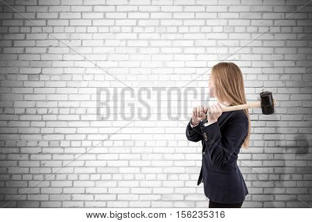 Side view of blond woman with sledgehammer about to smash white brick wall. Concept of no limits. Mock up