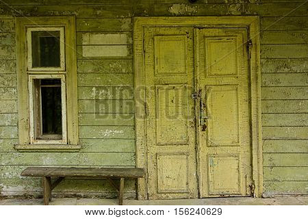 Wooden door on old wall at abandoned facade near wooden bench and window