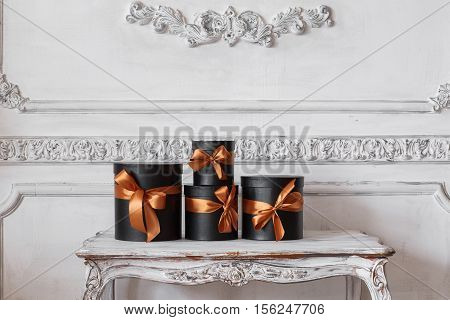 Wrapped gift black boxes with ribbons as Christmas presents on a table on luxury white wall design bas-relief stucco mouldings roccoco elements.