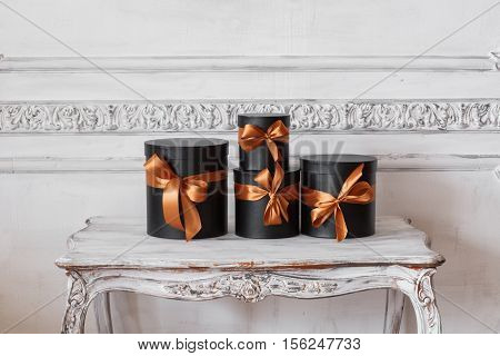 Wrapped gift black boxes with ribbons as Christmas presents on a table on luxury white wall design bas-relief stucco mouldings roccoco elements.